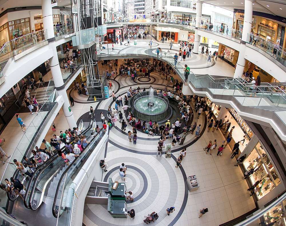 O interior movimentado do shopping Toronto Eaton Centre, com diversas lojas e pessoas passeando.