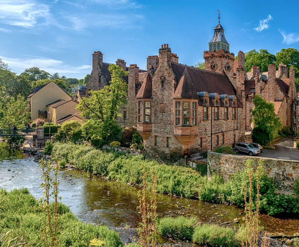 Edifícios históricos de pedra ao lado de um rio em um cenário verde, no bairro Dean Village, em Edimburgo, Escócia.
