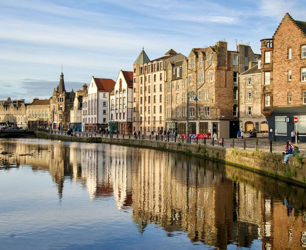 Fachada de edifícios históricos refletida na água ao longo da rua Shore, no bairro de Leith, em Edimburgo, Escócia.