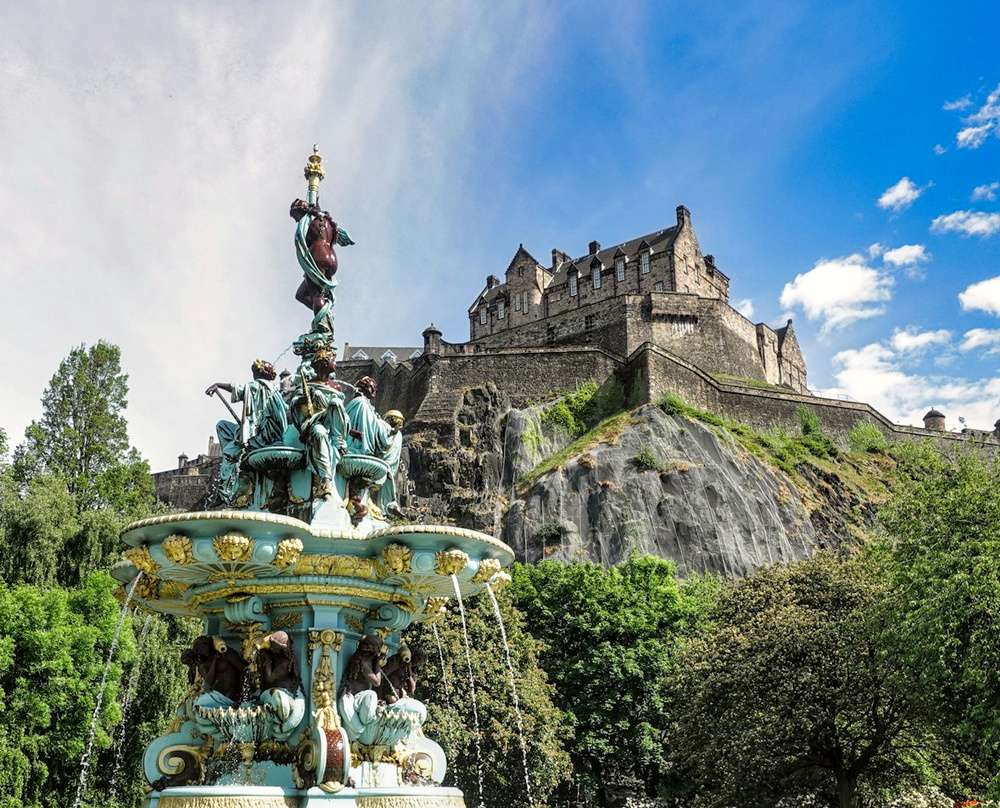 Vista encantadora do Castelo de Edimburgo sobre uma alta colina, e uma fonte colorida e detalhada em primeiro plano.