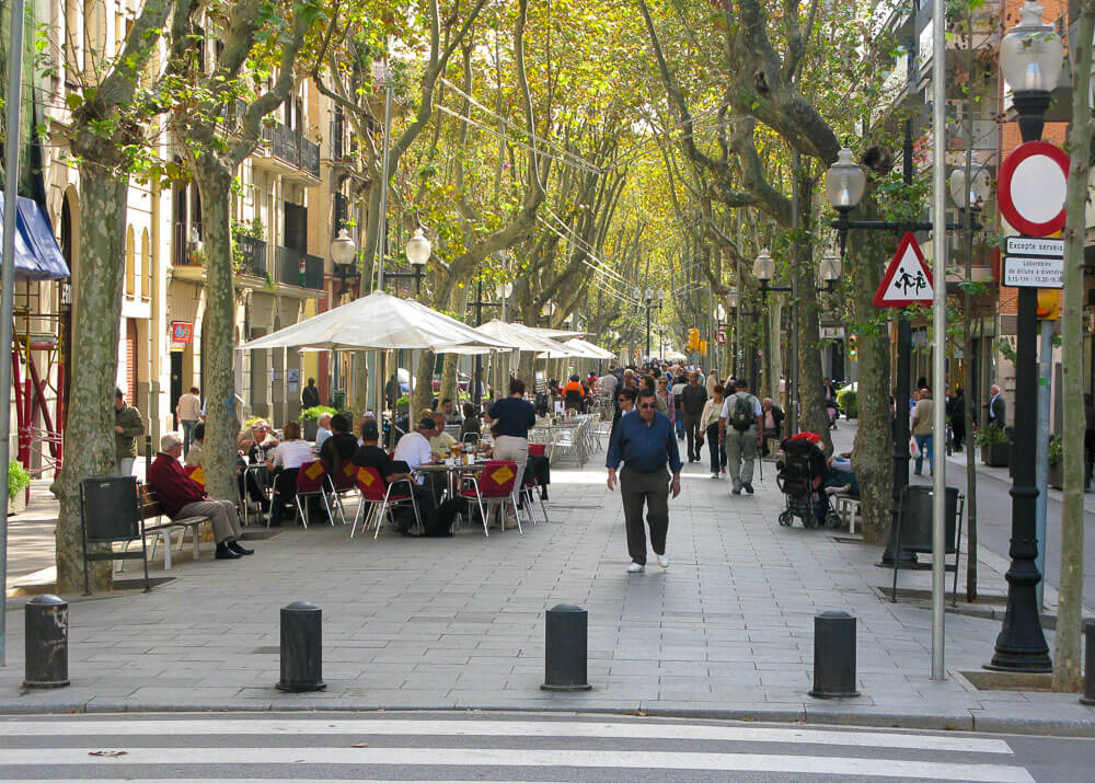 Rambla del Poblenou com várias mesas e cadeiras e muitas pessoas caminhando.
