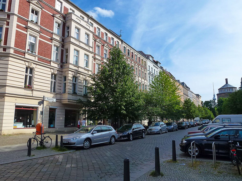 Rua tranquila e arborizada em Prenzlauer Berg, Berlim, com prédios residenciais de estilo clássico.