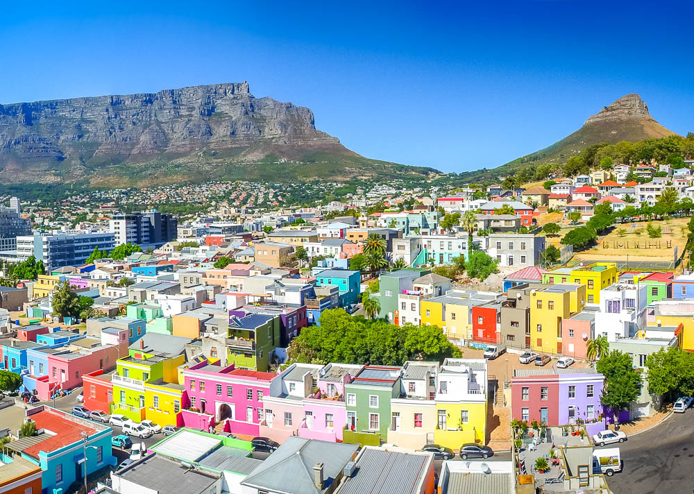 Casas coloridas do bairro Bo-Kaap em frente à paisagem montanhosa de Cape Town, com a imponente Table Mountain ao fundo e colinas suaves ao redor.