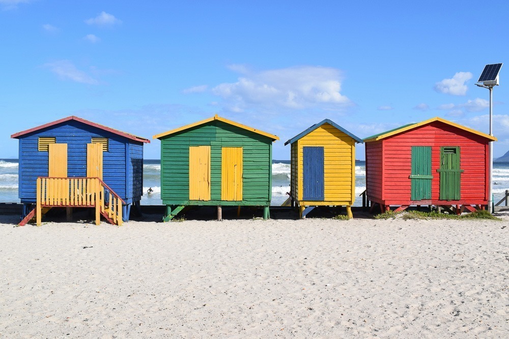 Quatro casinhas coloridas na Praia de Muzeinberg, em Cape Town.