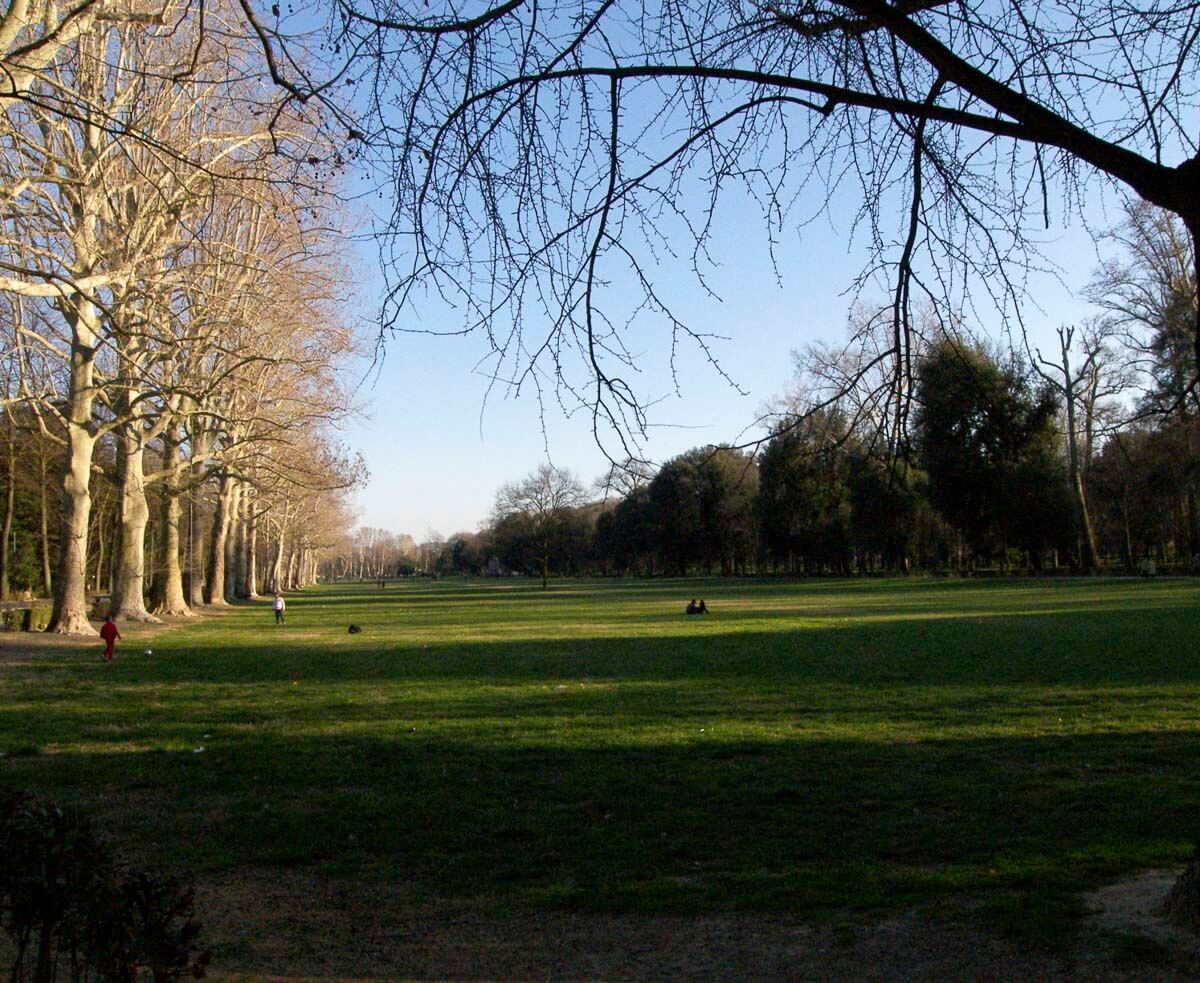 Extensa área verde do Parco delle Cascine, com árvores alinhadas ao fundo.