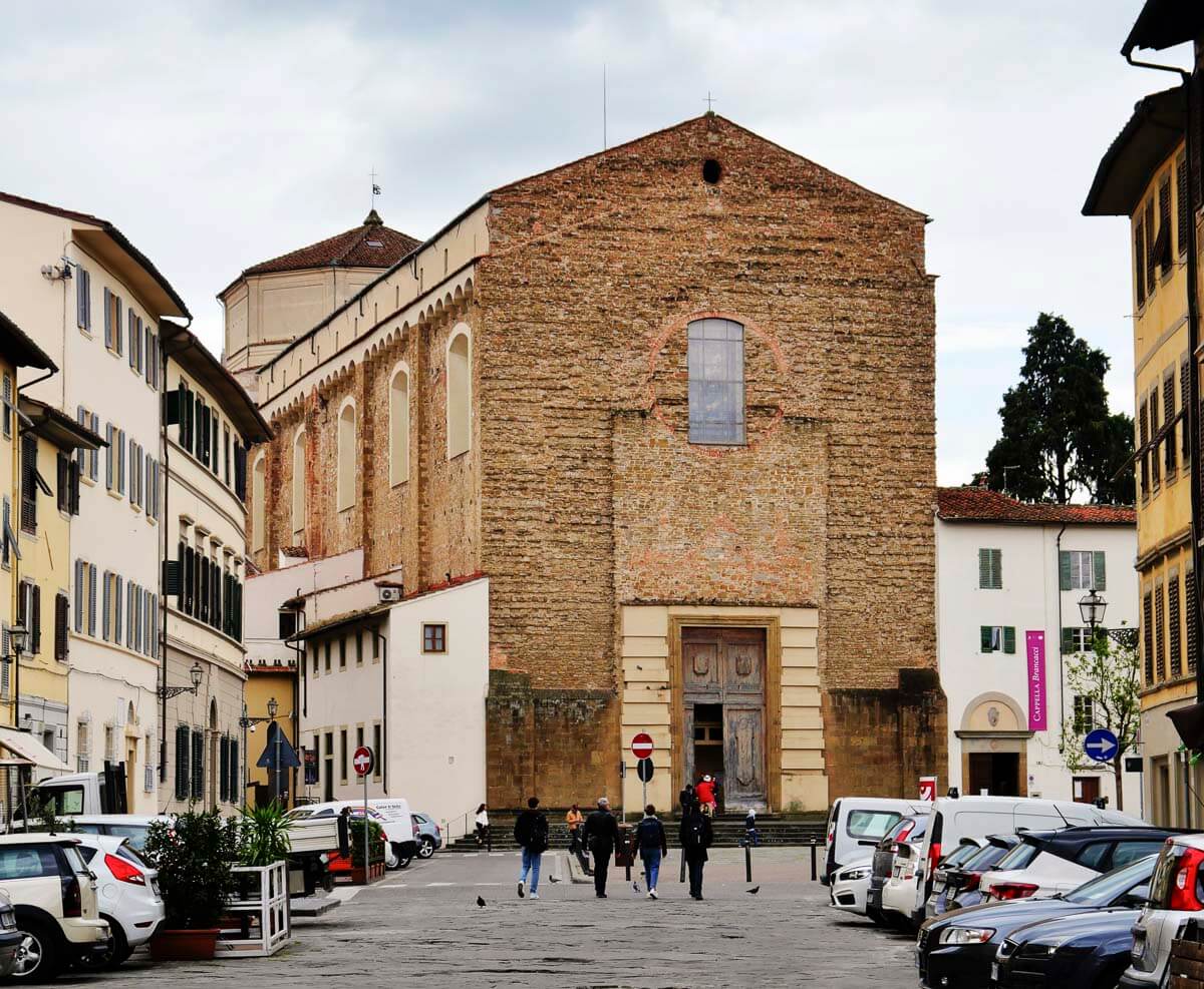 Fachada da Igreja de Santa Maria del Carmine no bairro San Frediano, em Florença, cercada por edifícios históricos e carros estacionados.