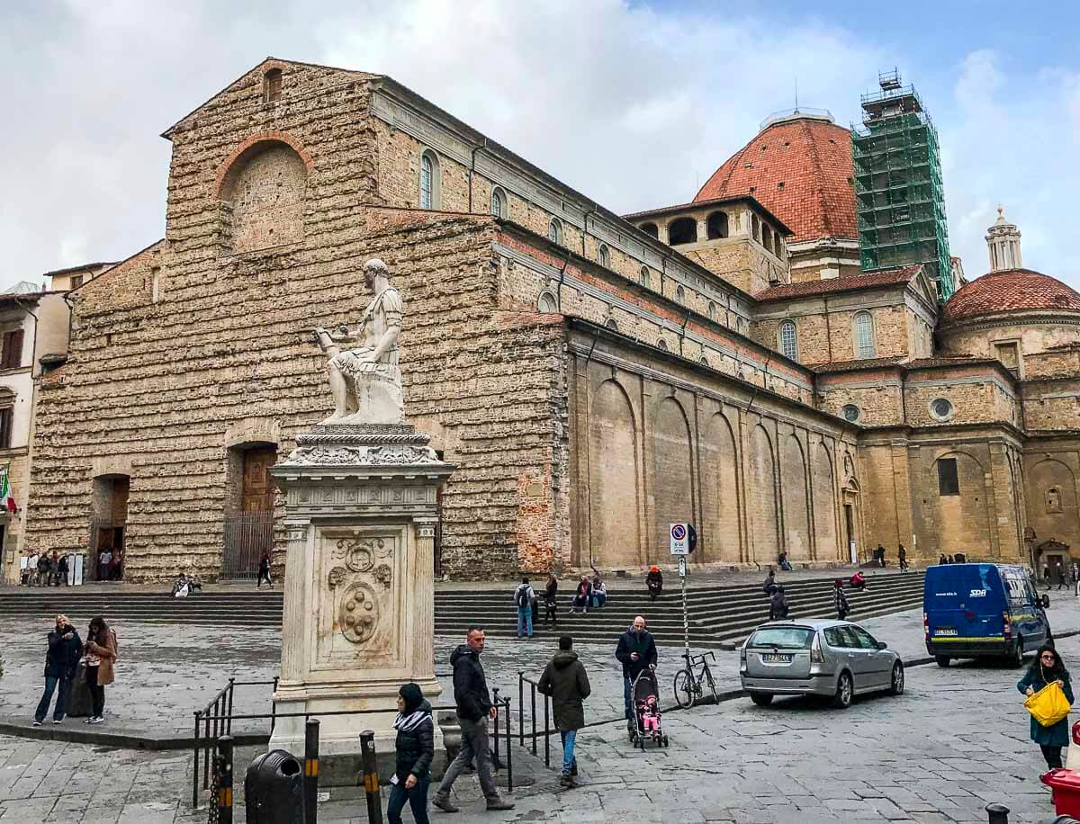 Basílica de San Lorenzo em Florença, com fachada de pedra e escultura de mármore em destaque na praça.