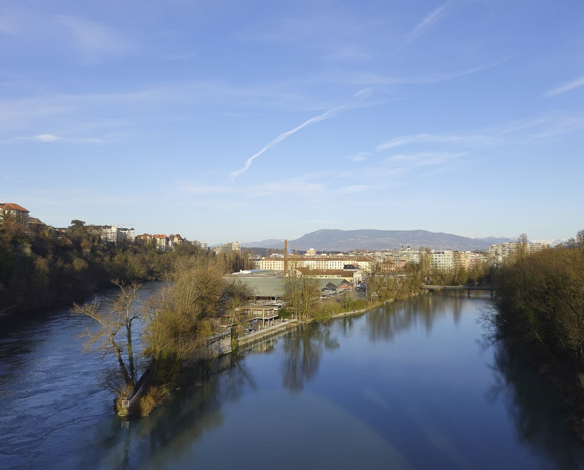 Vista panorâmica do encontro dos rios Rhône e Arve em Genebra, cercado por vegetação e prédios ao fundo.