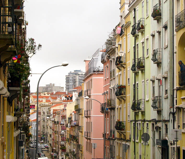 Rua estreita de Arroios, em Lisboa, com prédios coloridos de vários andares e varandas decoradas.