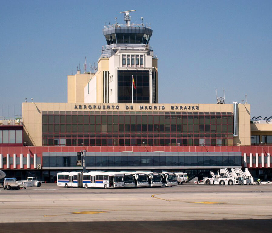 Vista do Aeroporto de Madrid-Barajas, com ônibus e veículos estacionados em frente ao terminal principal.