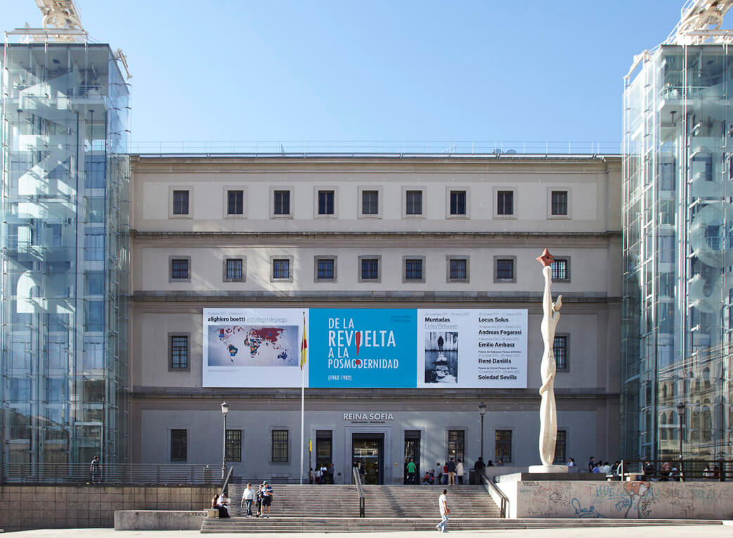 Fachada do Museu Reina Sofía em Madrid, com uma escultura alta na frente e banners de exposições visíveis.