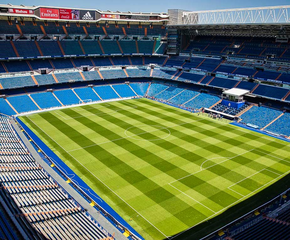 Vista aérea do Estádio Santiago Bernabéu, em Madrid, com arquibancadas vazias e gramado bem cuidado.