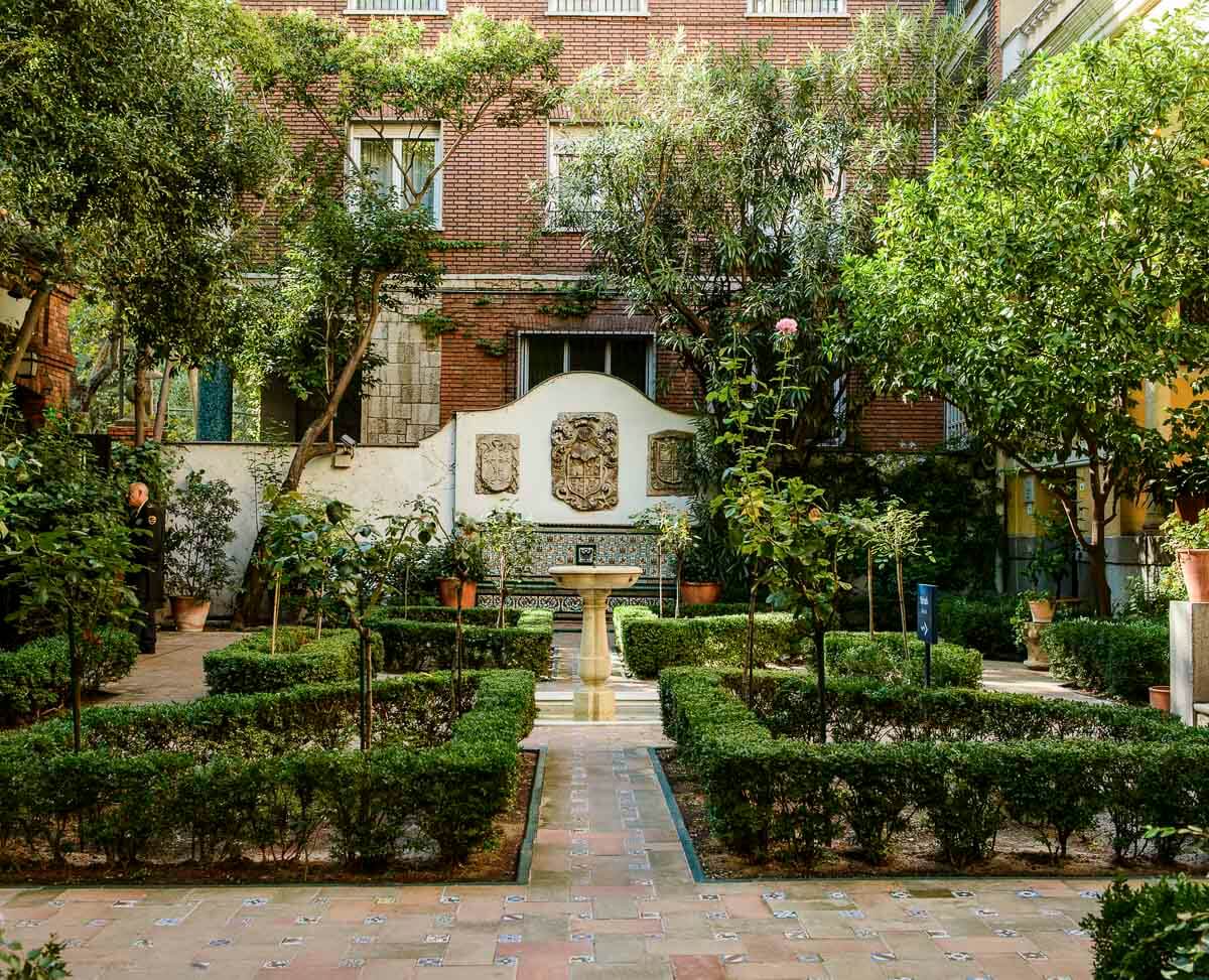 Jardim tranquilo do Museu Sorolla em Madrid, cercado de plantas e árvores, com uma fonte ao centro e paredes decoradas ao fundo.