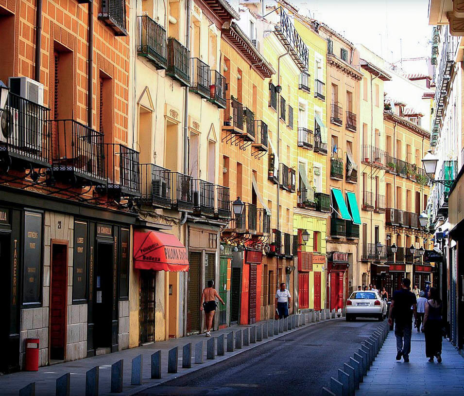 A Calle de la Cava Baja, uma rua de Madrid com prédios antigos e coloridos, lojas e algumas pessoas caminhando.