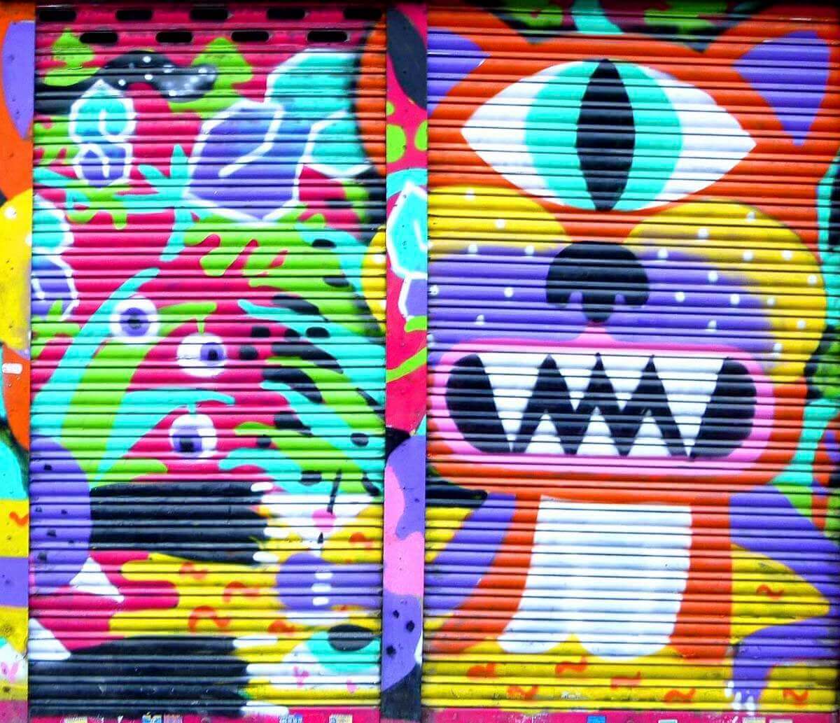 Arte de rua vibrante no bairro de Malasaña, Madrid, com um mural colorido de criaturas surreais em uma porta fechada de estabelecimento.
