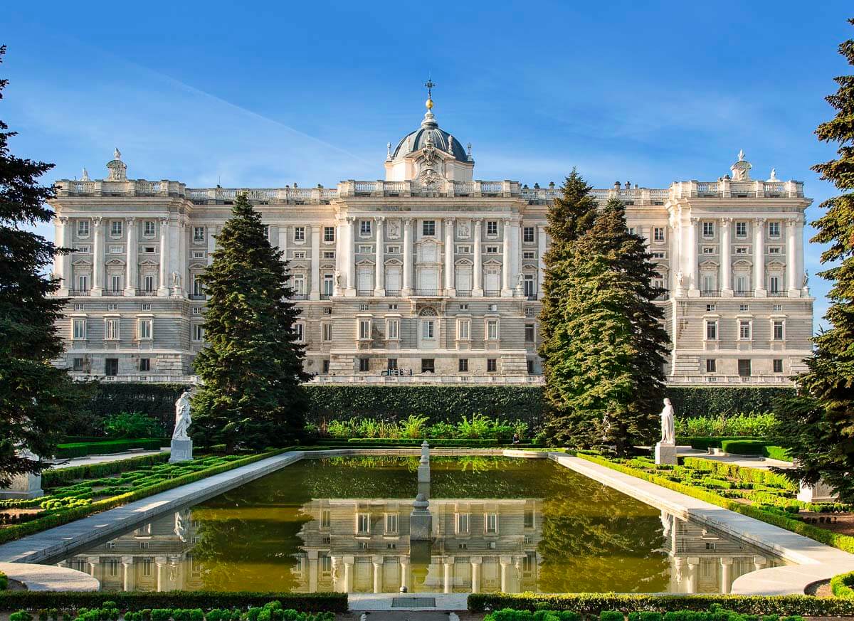 Palácio Real de Madrid com um jardim à frente, incluindo uma fonte e estátuas.