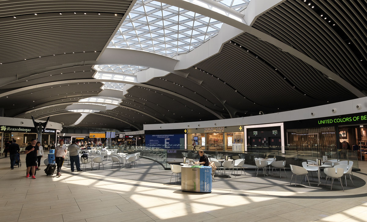 Interior moderno do aeroporto de Roma, com teto curvado e luz natural.