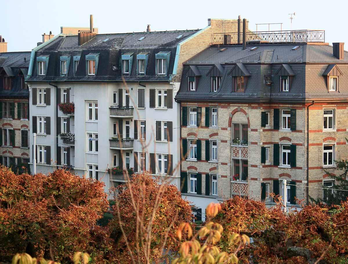 Fachadas de edifícios residenciais com arquitetura clássica e detalhes de tijolos em uma rua arborizada do bairro de Fluntern, Zurique.
