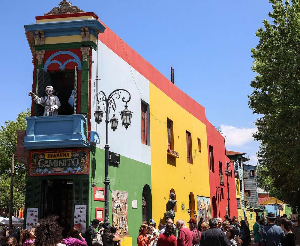 Fachada de um prédio com cores vibrantes em amarelo, azul, vermelho e verde, representando a rua turística Caminito em Buenos Aires.