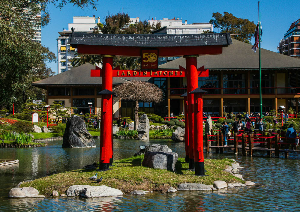 Portal Torii vermelho no Jardim Japonês de Buenos Aires, em meio a um lago cercado de pedras e árvores ornamentais.