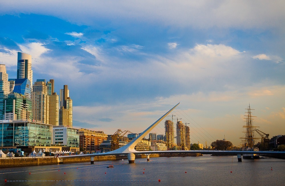 Puente de la Mujer sobre um extenso rio de águas escuras, com prédios modernos ao fundo.