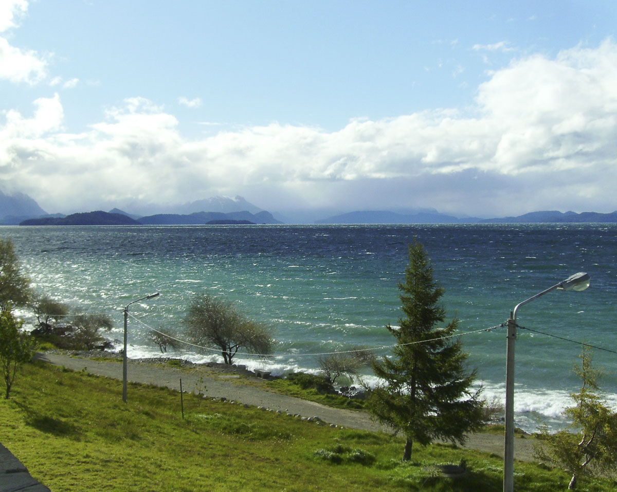 Vista do Lago Nahuel Huapi com montanhas ao fundo em um dia parcialmente nublado.