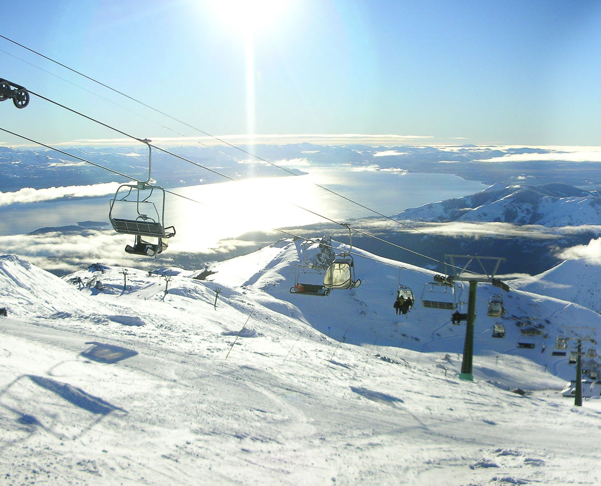 Vista do alto do Cerro Catedral, com teleféricos e montanhas cobertas de neve.