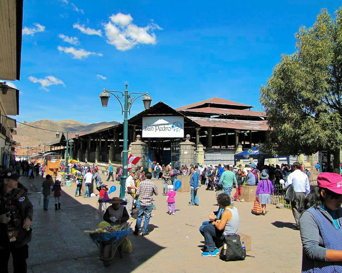 Entrada movimentada do Mercado Central de San Pedro, com pessoas comprando e vendendo produtos ao ar livre.