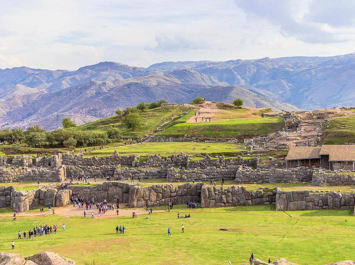 Ruínas de Sacsayhuamán, com pedras gigantes formando muralhas e montanhas ao fundo.