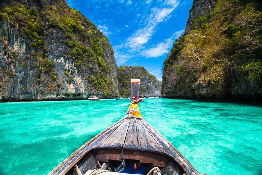 Proa de um barco tailandês apontando para águas cristalinas cercadas por penhascos verdes e imponentes nas Ilhas Phi Phi.