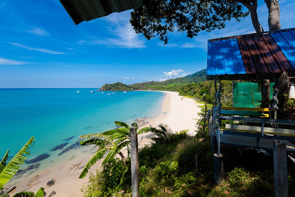Praia de Kantiang Bay vista de uma colina, com mar azul-turquesa e faixa de areia branca cercada por vegetação exuberante.