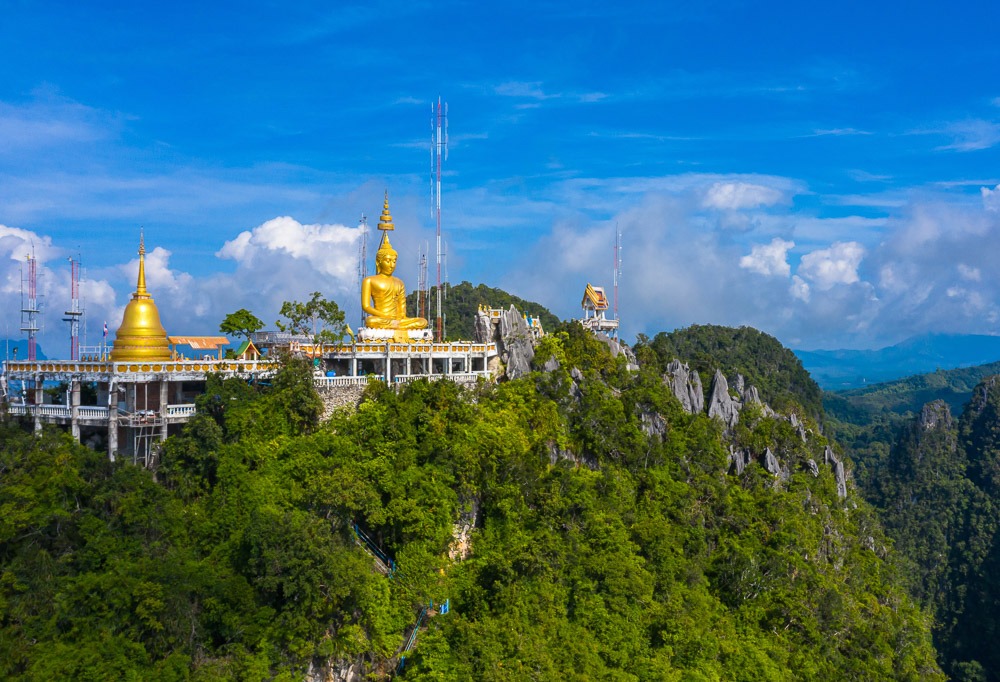 Grande estátua dourada de Buda no topo de uma montanha verdejante, parte do Templo da Caverna do Tigre em Krabi.