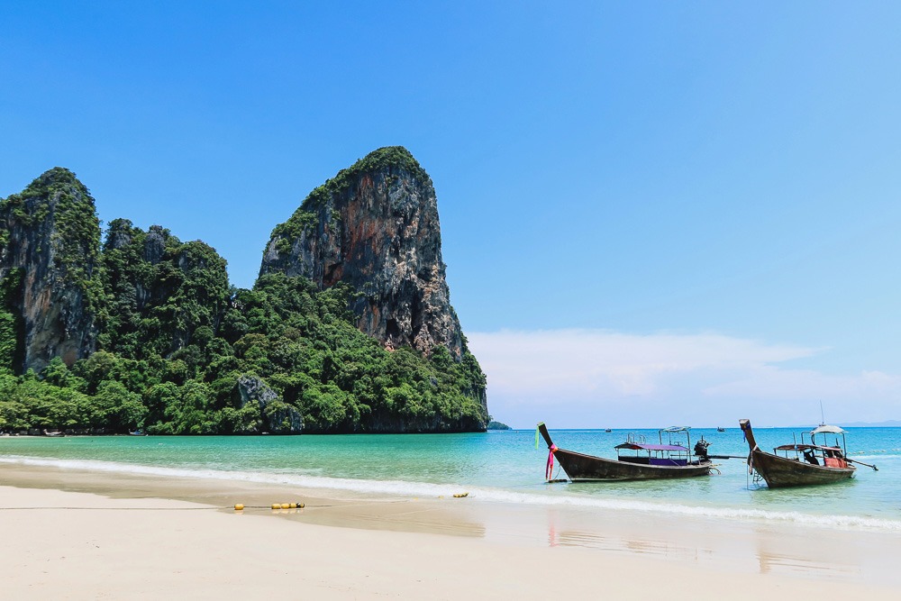 Praia de Railay com uma enorme formação rochosa à esquerda, areia dourada e mar azul cristalino.