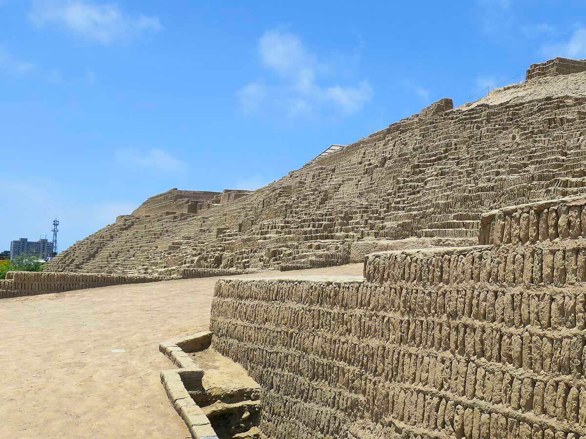 Ruínas da Huaca Pucllana em Lima, com paredes de adobe dispostas em níveis e degraus, em um dia de céu azul claro.