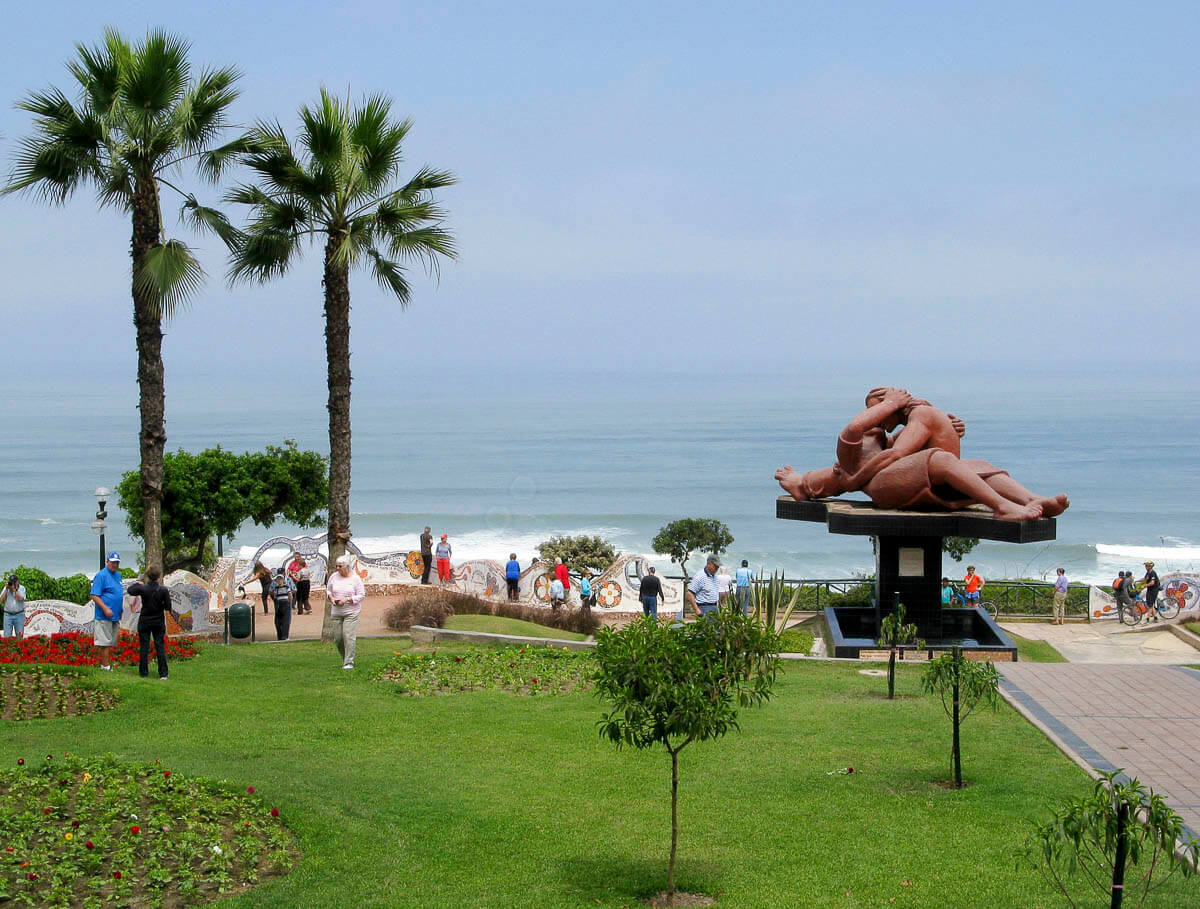 Parque del Amor no Malecón de Lima, com uma escultura de um casal abraçado, palmeiras, flores e vista para o mar.