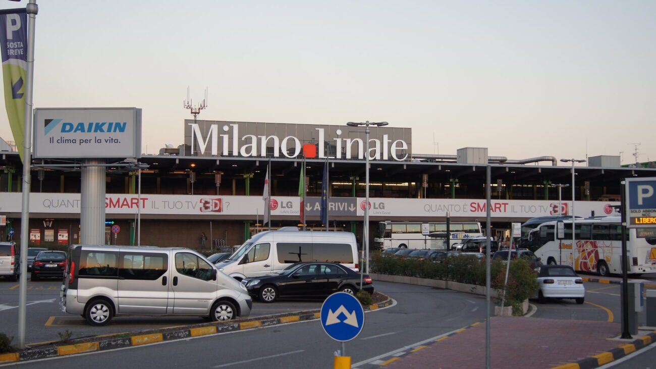 Entrada principal do Aeroporto de Linate em Milão, com carros estacionados em frente.