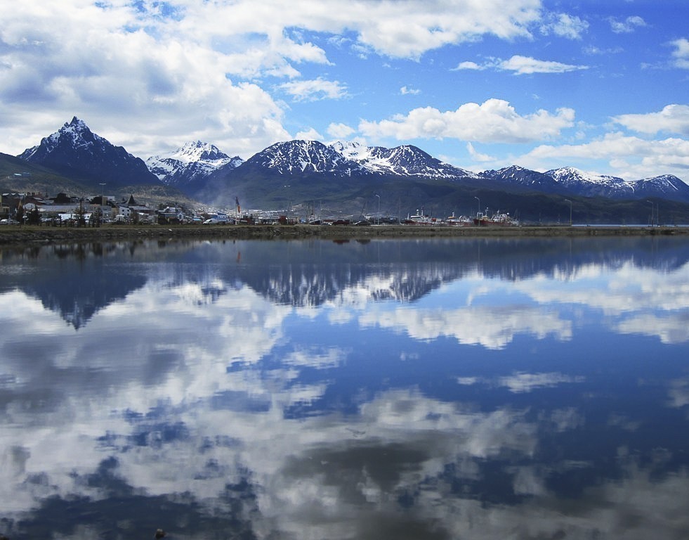 Reflexo das montanhas e do céu azul com nuvens na calma água da Bahia Encerrada, em Ushuaia.