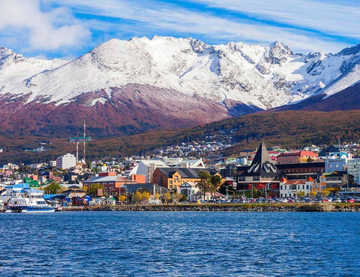 Vista do centro de Ushuaia com casas coloridas e montanhas cobertas de neve ao fundo, refletindo a beleza da Patagônia.