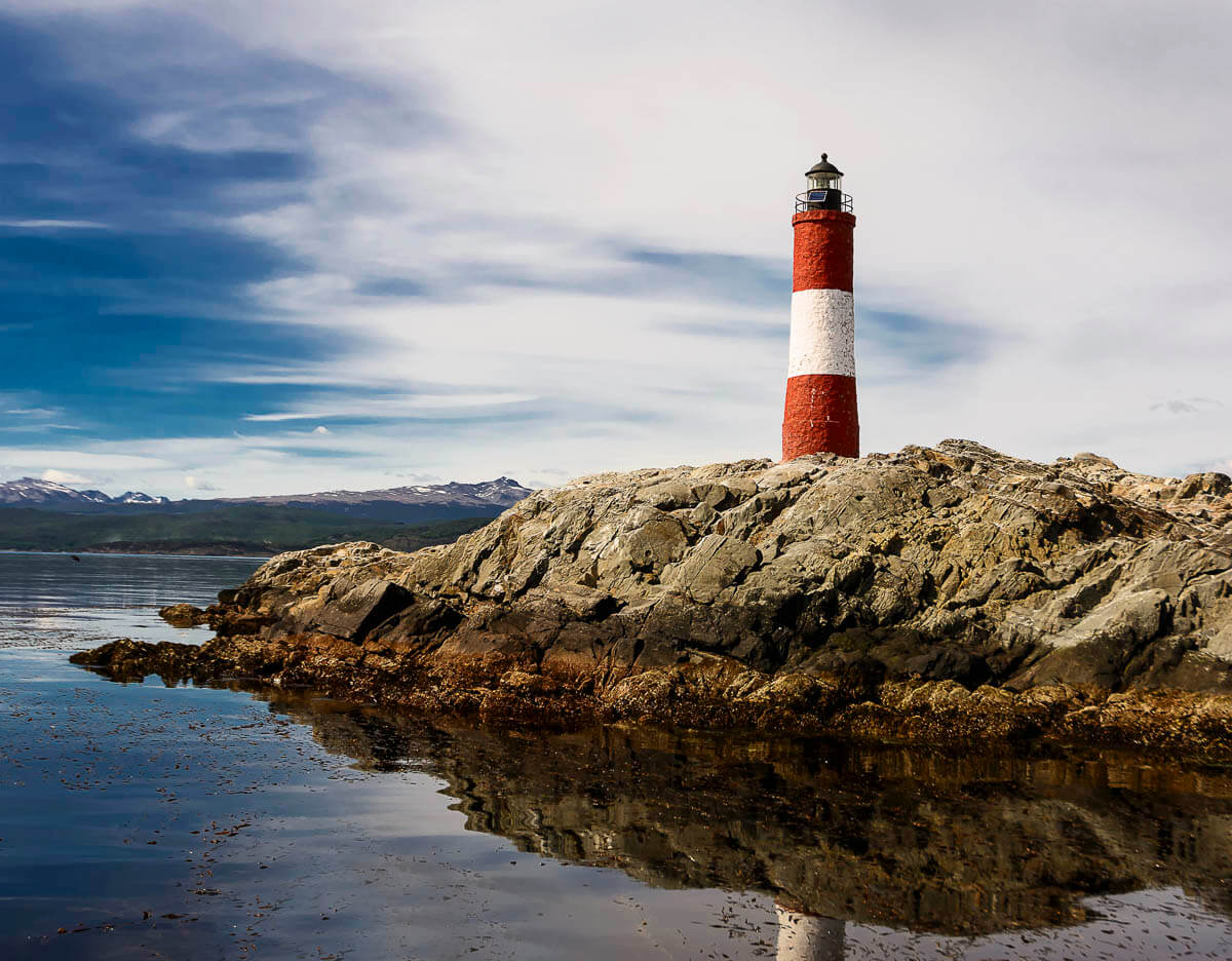 Farol Les Éclaireurs em Ushuaia, localizado em uma pequena ilha rochosa, com céu parcialmente nublado ao fundo.