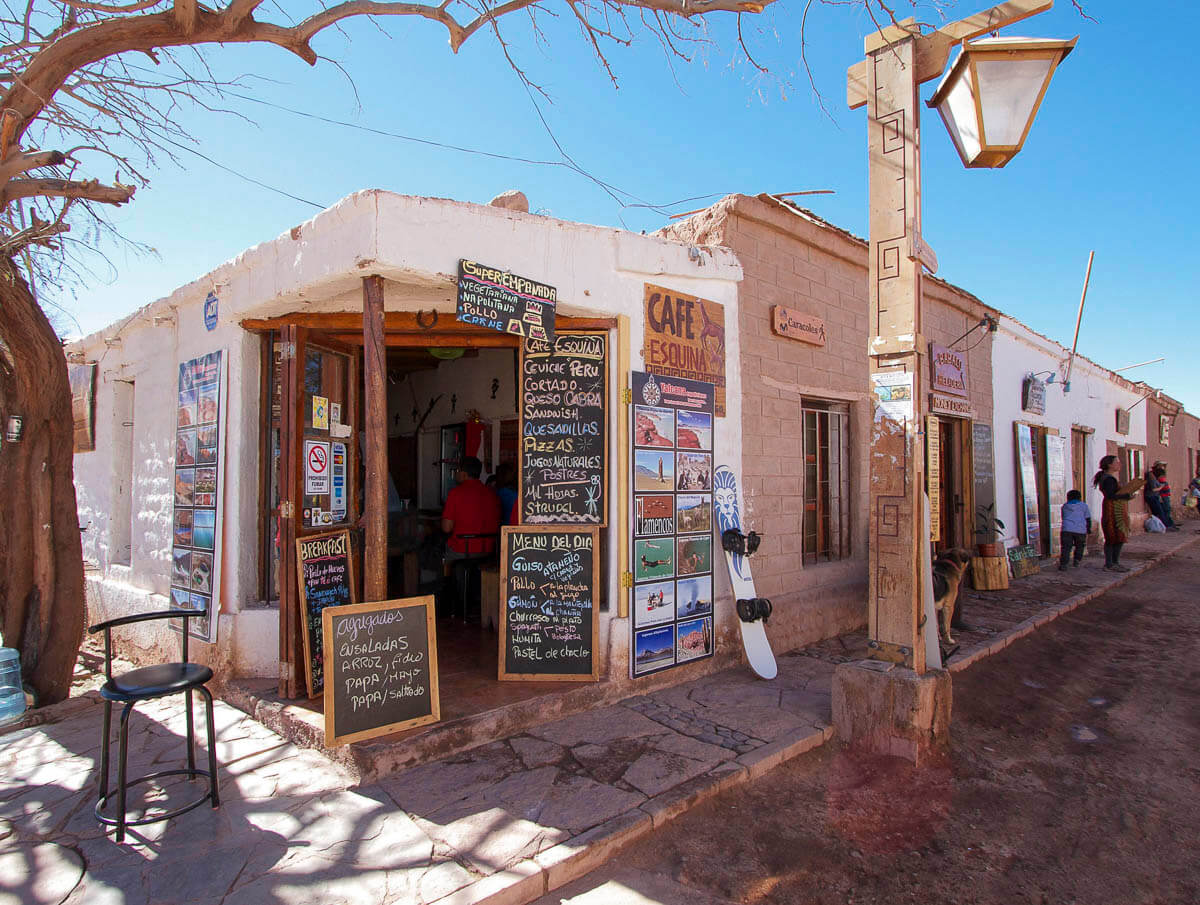 A central Rua Caracoles em San Pedro de Atacama, com construções rústicas e um café.