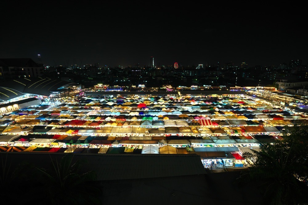 Vista aérea e noturna do Train Night Market Ratchada, com muitas barracas iluminadas.