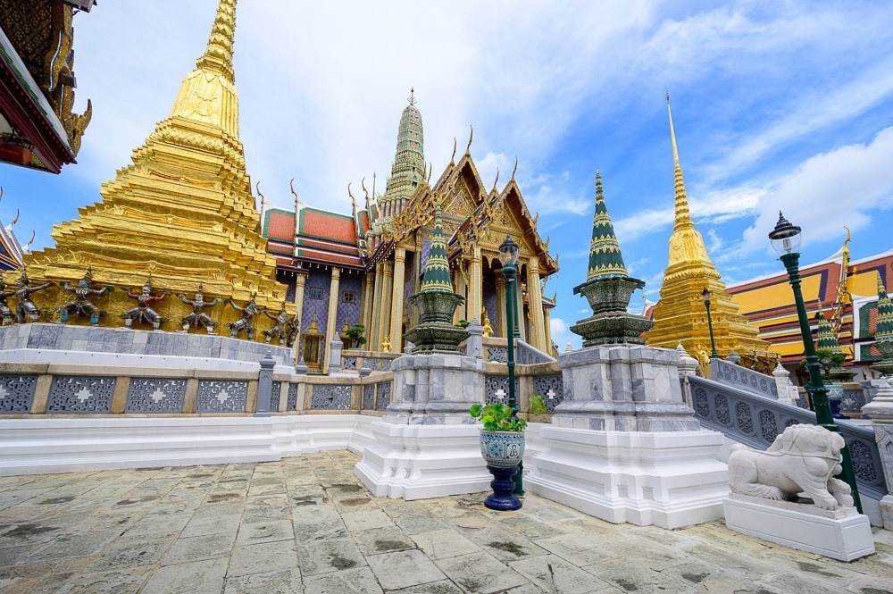 Vista diurna e parcialmente lateral para o Templo do Buda de Esmeralda (War Phra Kaew), com torres pontudas e douradas.