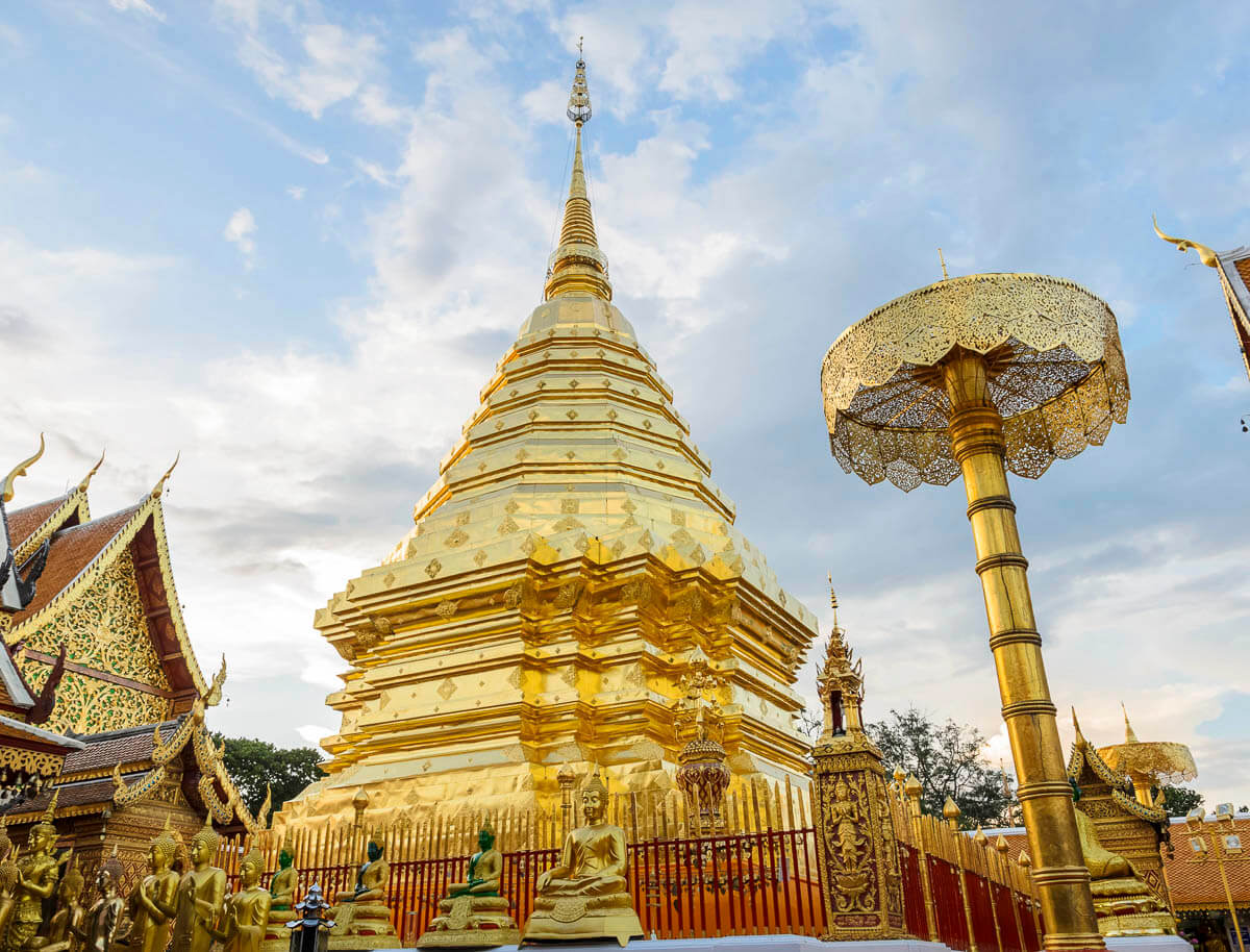 Pagoda dourada do Wat Phra That Doi Suthep na montanha Suthep, cercado por estátuas de Buda e céu azul.