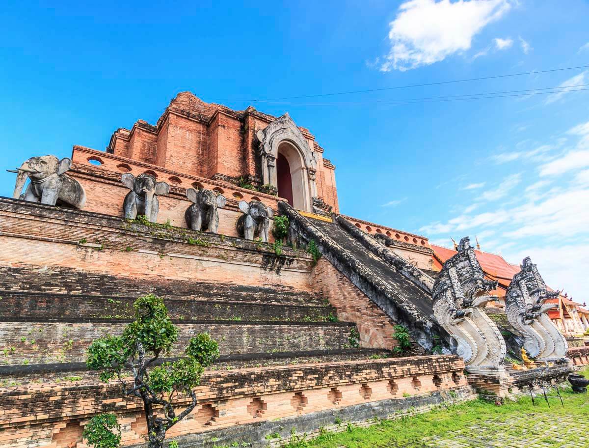 Templo histórico Wat Chedi Luang em Chiang Mai, com escadarias de tijolos e esculturas de elefantes.