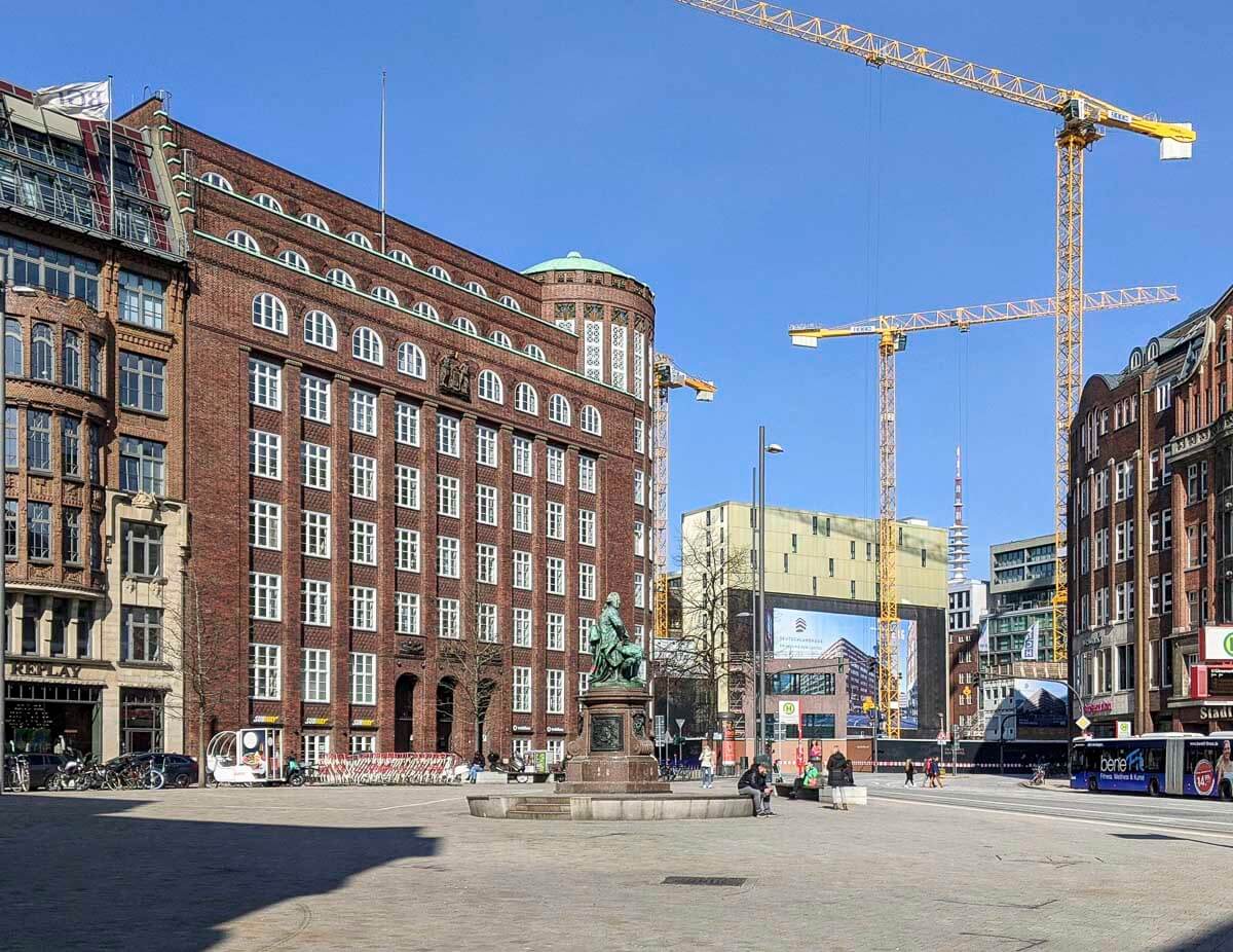 Praça em Hamburgo com gruas de construção ao fundo e prédios históricos ao redor.