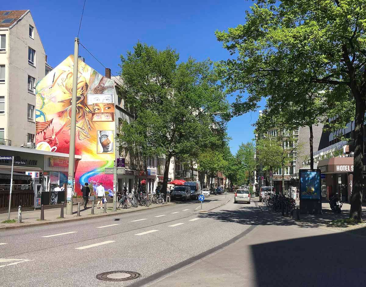 Rua no bairro de St. Georg, em Hamburgo, com murais coloridos e árvores alinhadas.