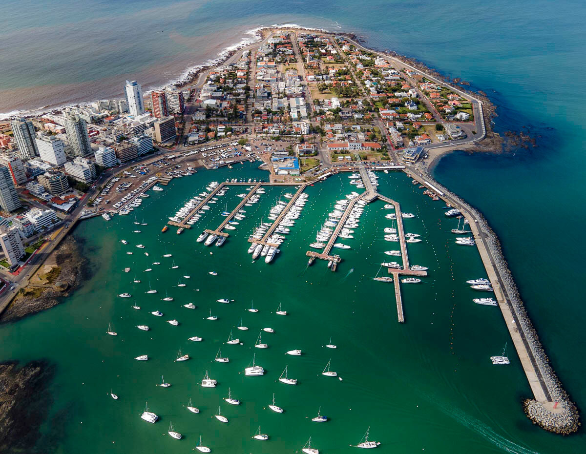 Vista aérea da península de Punta del Este com uma marina cheia de iates e barcos cercados por águas turquesa.