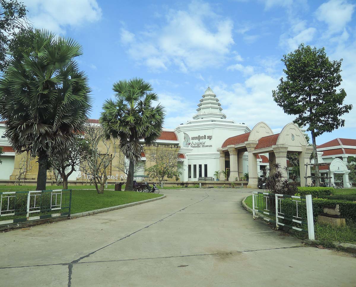 Entrada do Angkor National Museum, em Siem Reap, com arquitetura branca e telhados vermelhos rodeada por árvores e gramados bem cuidados.