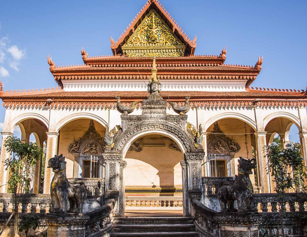 Templo Wat Bo em Siem Reap, com arquitetura tradicional e estátuas de leões decorando a entrada, cercado por vegetação.