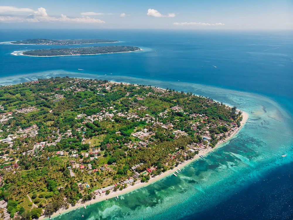 Vista aérea das Ilhas Gili, com águas azul-turquesa, vegetação exuberante e pequenas praias de areia branca.